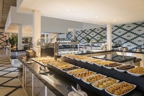 A buffet with various food items, a tiled floor, and a modern kitchen area in the background.