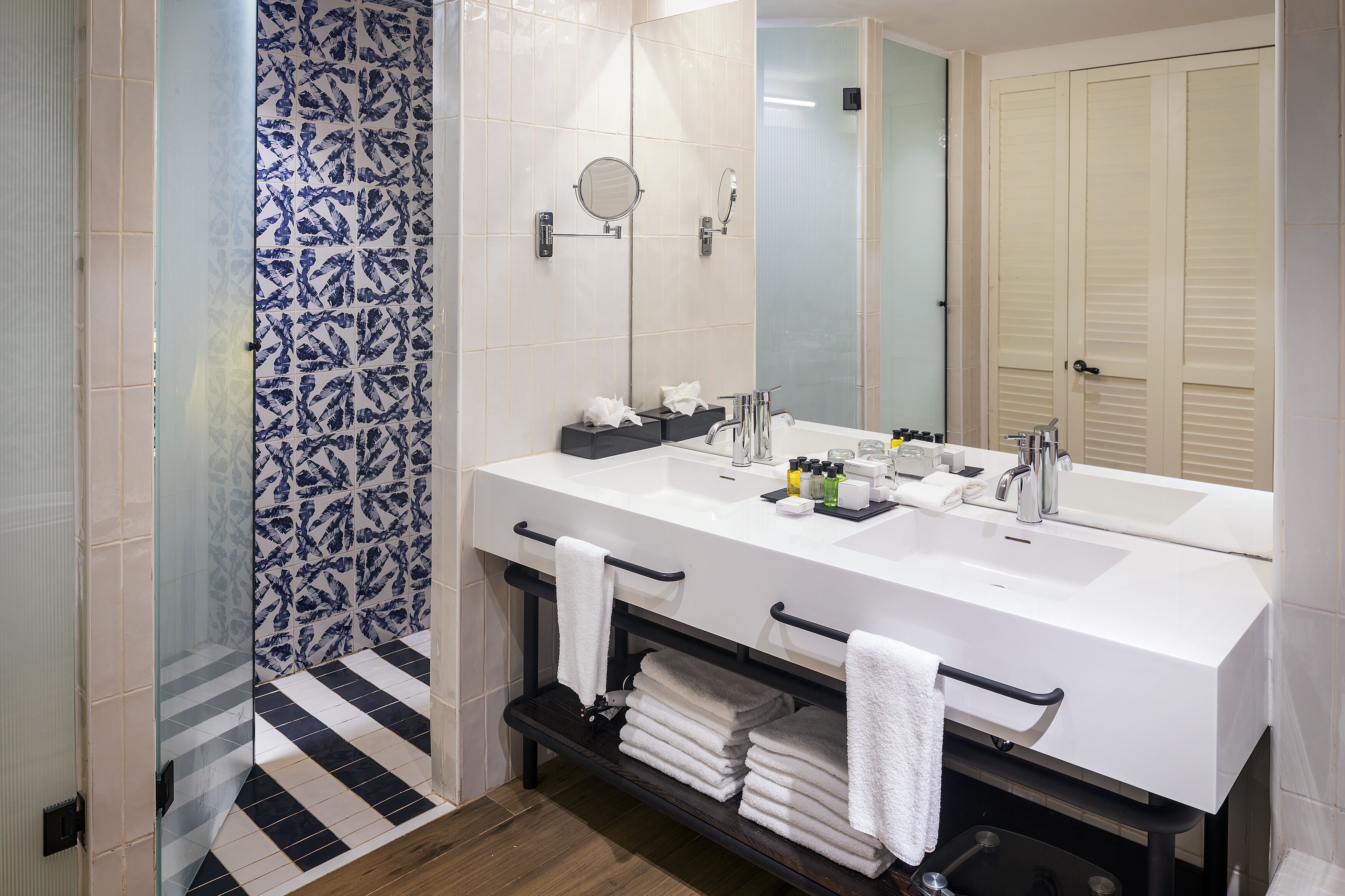 A bathroom with a large white sink, two mirrors, a glass shower enclosure, and a towel rack with folded towels.