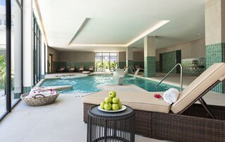 Una piscina interior con sillones de descanso y una mesa de mimbre con manzanas y flores.
