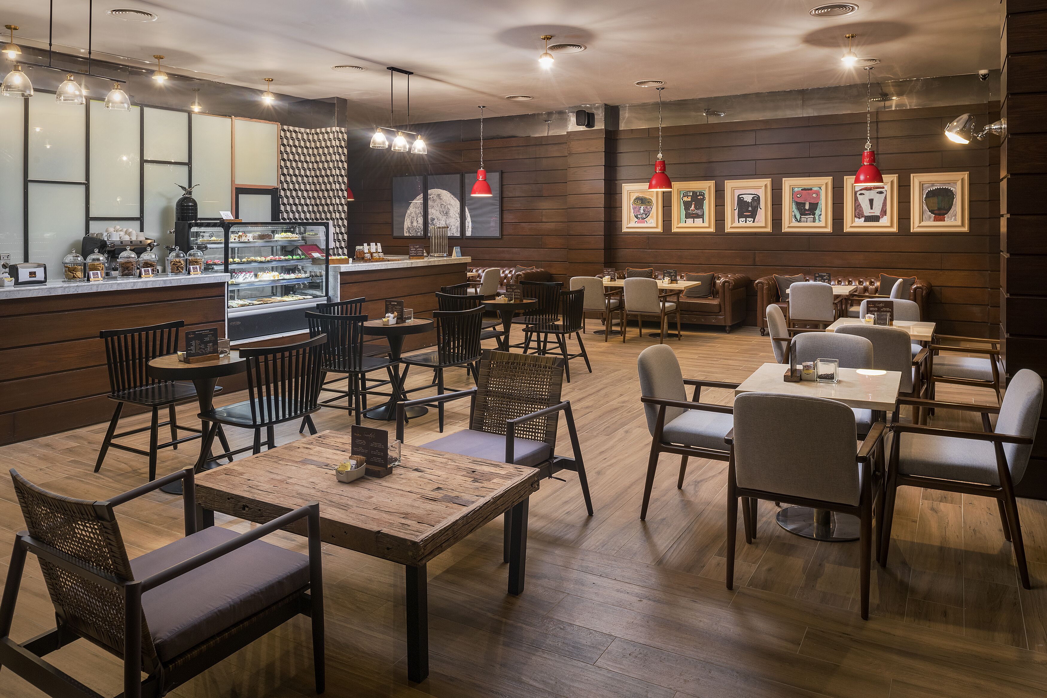 A restaurant with wooden flooring, black and grey chairs, and red pendant lights.