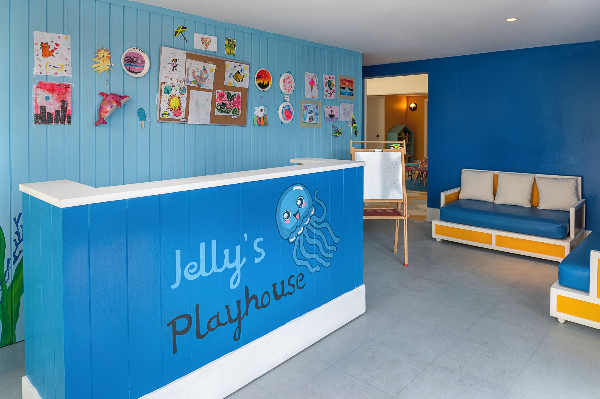 A reception desk with a blue and white color scheme, a wall decorated with children's artwork, and a blue sofa in the background.