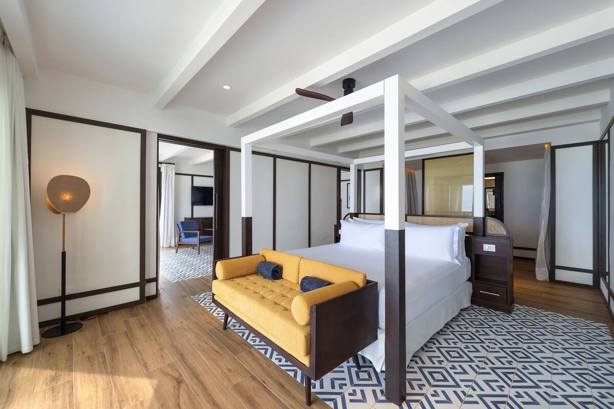 Una habitación de hotel moderna con una cama con dosel, un sofá cama, una mesita de noche y una lámpara de pie.