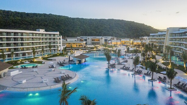 Um resort com várias piscinas, espreguiçadeiras e vista para uma colina arborizada.