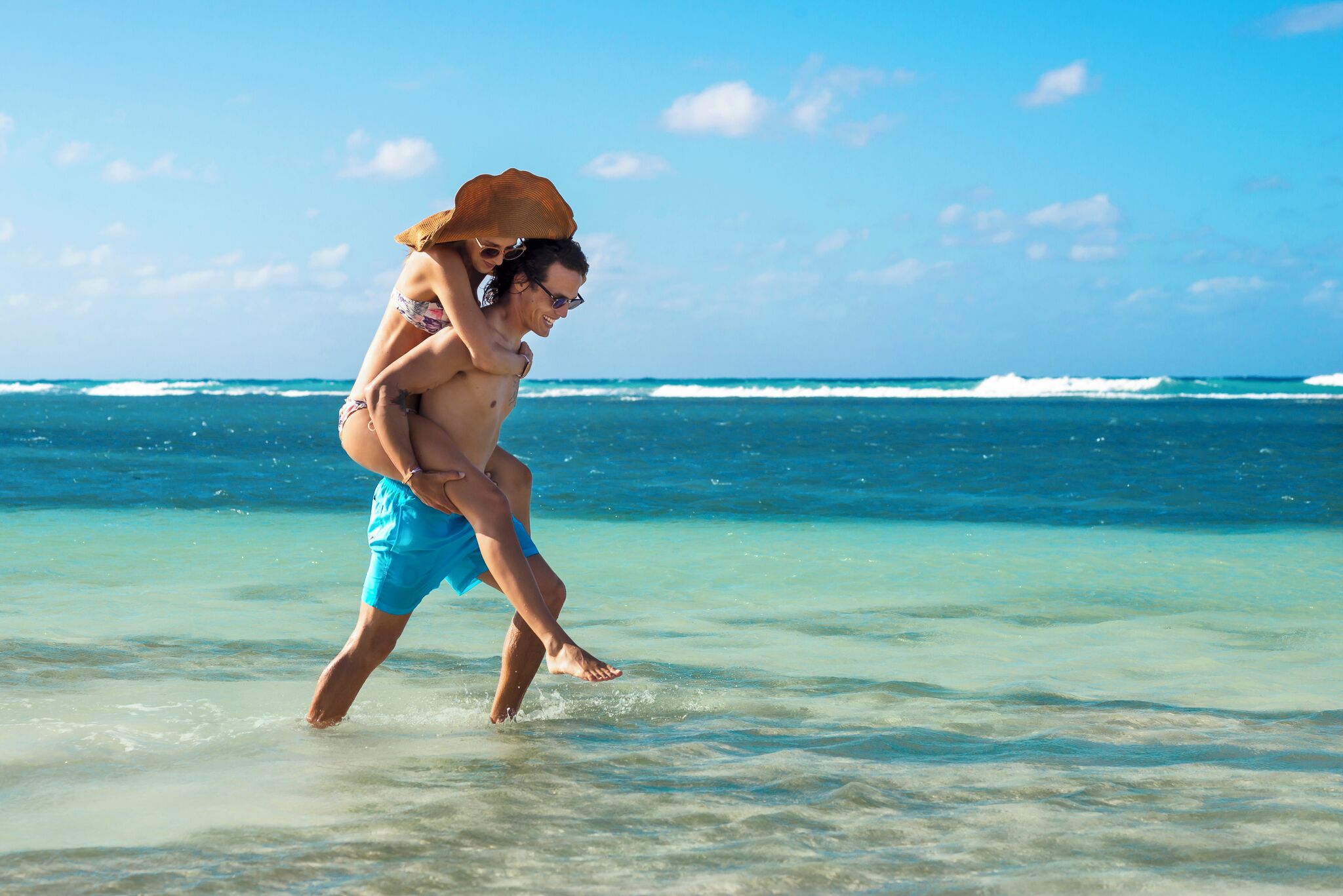 A beach scene with clear water and a person carrying another on their shoulders.