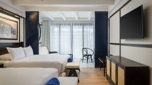 A hotel room with two beds, a desk, a chair, a TV, and a large window with curtains.
