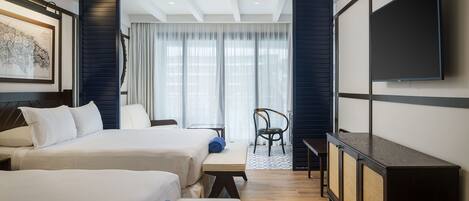 A hotel room with two beds, a desk, a chair, a TV, and a large window with curtains.