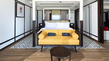 Une chambre d’hôtel moderne avec un lit, un canapé jaune, une petite table et un tapis à motifs.