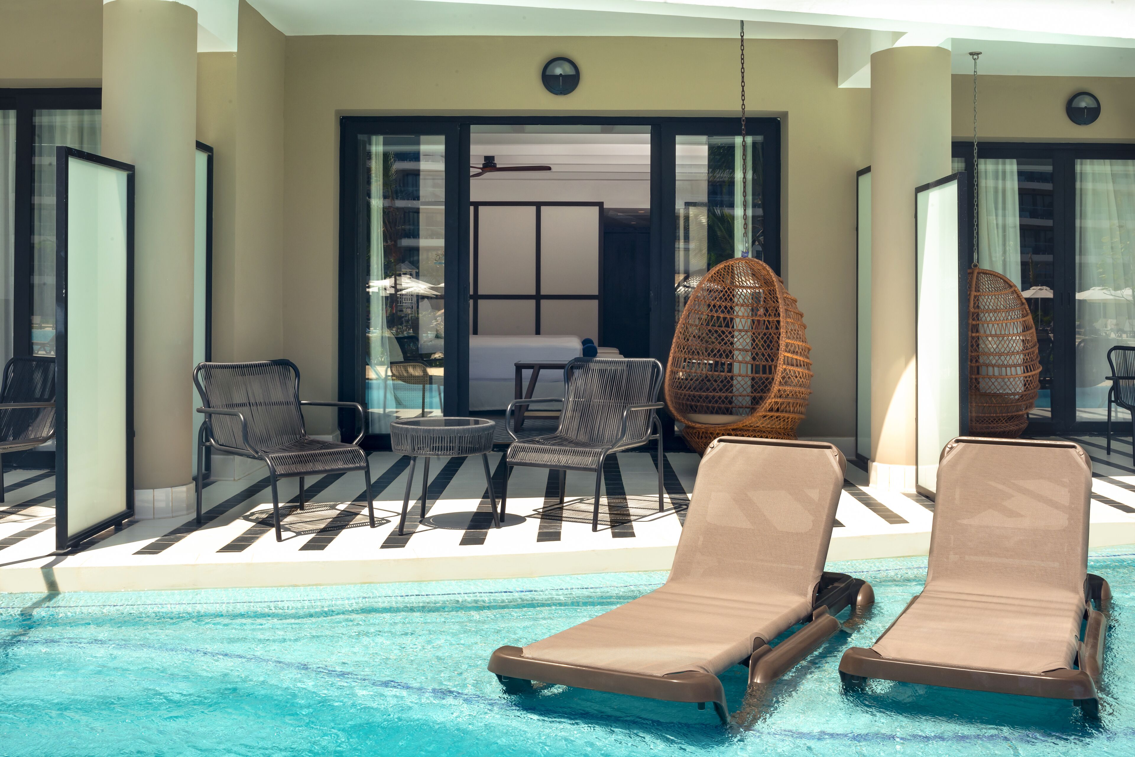 A poolside area with lounge chairs, a table, and wicker chairs.