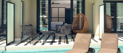 A poolside area with lounge chairs, a table, and wicker chairs.