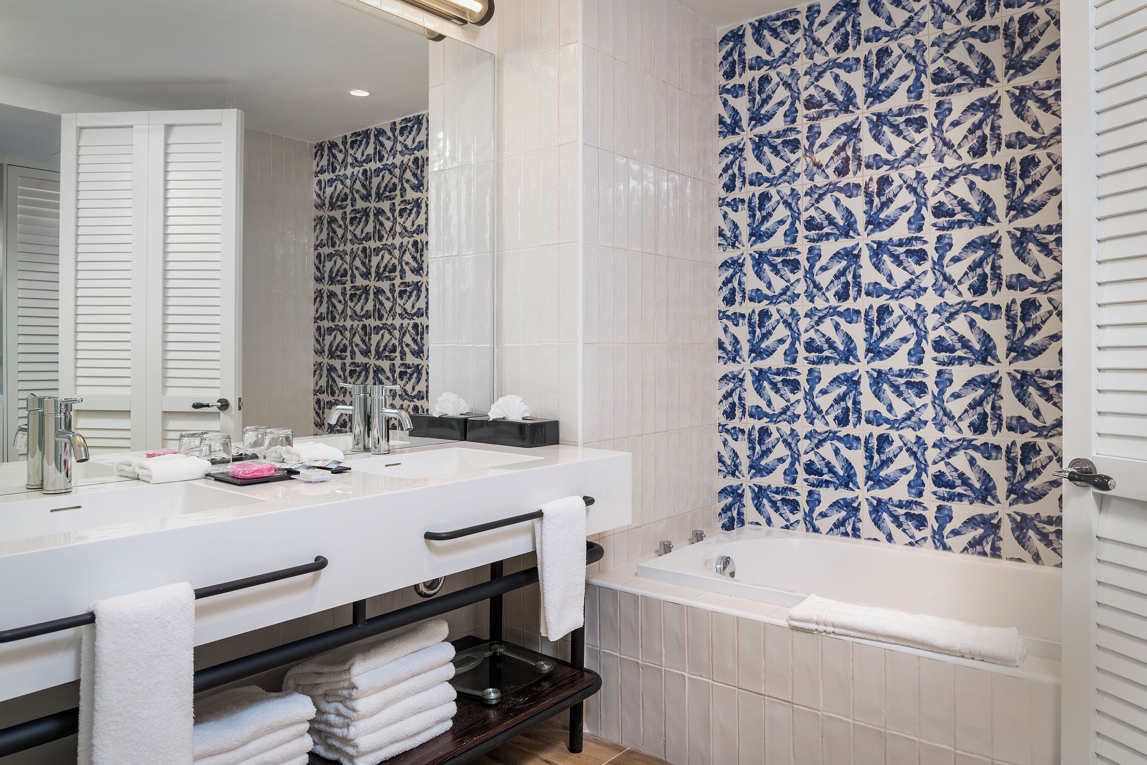 A bathroom with a white sink, black towel rack, and a blue patterned shower wall.