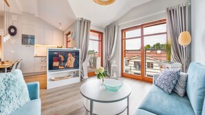 A modern living room with a sofa, a coffee table, and a TV. There is a kitchen area with cabinets and a dining table. - Apartamenty Sun & Snow Neptun Park (Gdansk)