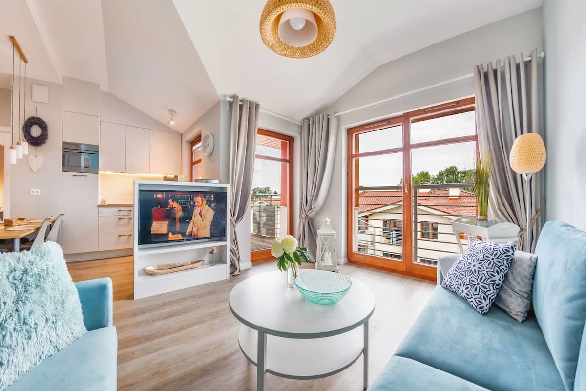 Una sala de estar moderna con un sofá, una mesa de centro y un televisor. Hay una zona de cocina con armarios y una mesa de comedor.