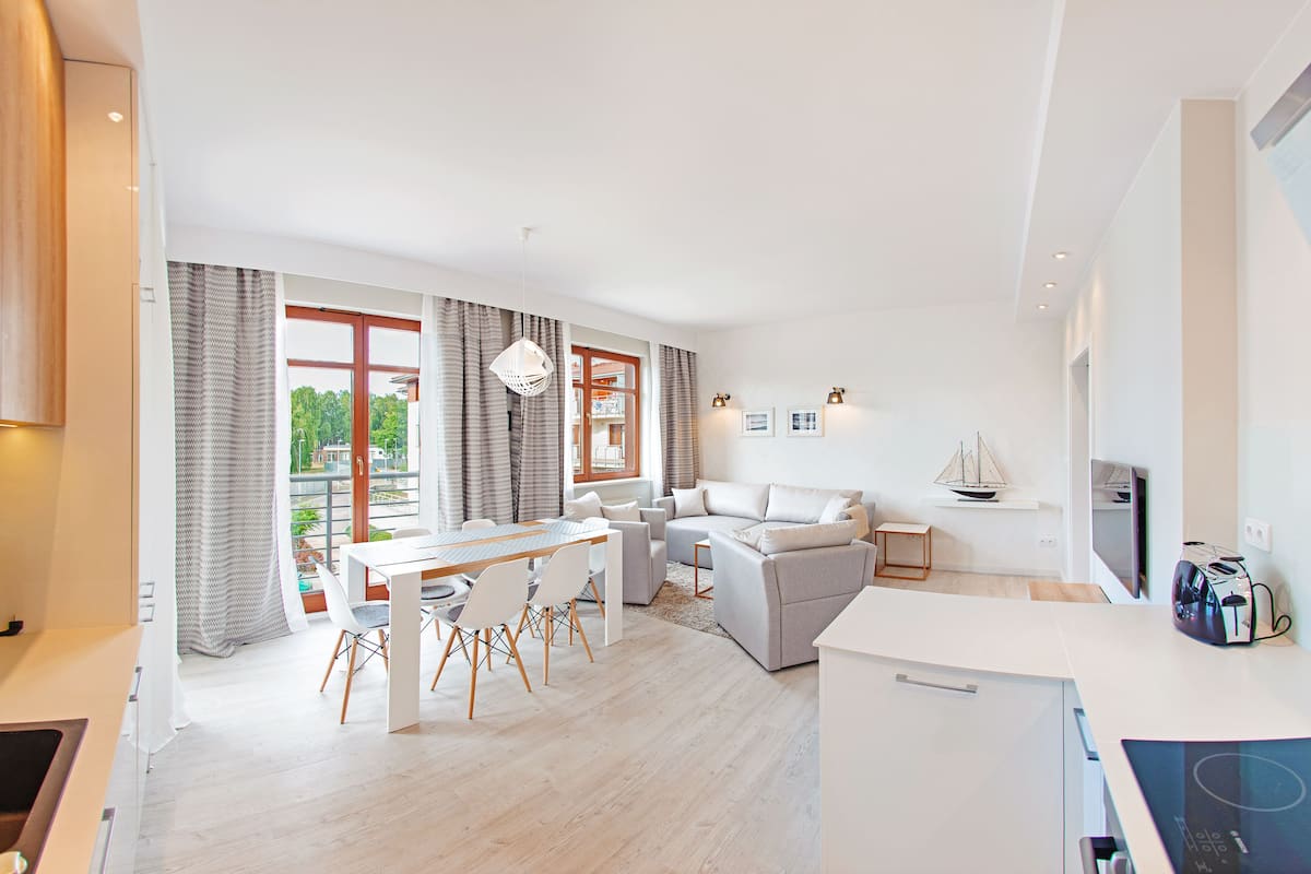 Una sala de estar moderna con comedor, ventanas amplias y una cocina.