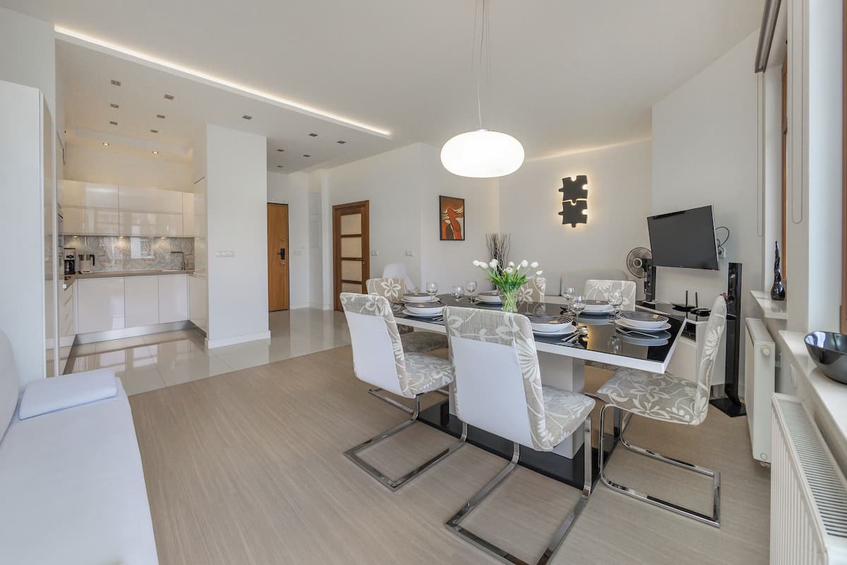 Un comedor moderno con una mesa central dispuesta para seis personas, rodeada de sillas blancas tapizadas.