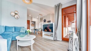 A modern living room with a blue sofa, a white coffee table, and a television. - Apartamenty Sun & Snow Neptun Park (Gdansk)