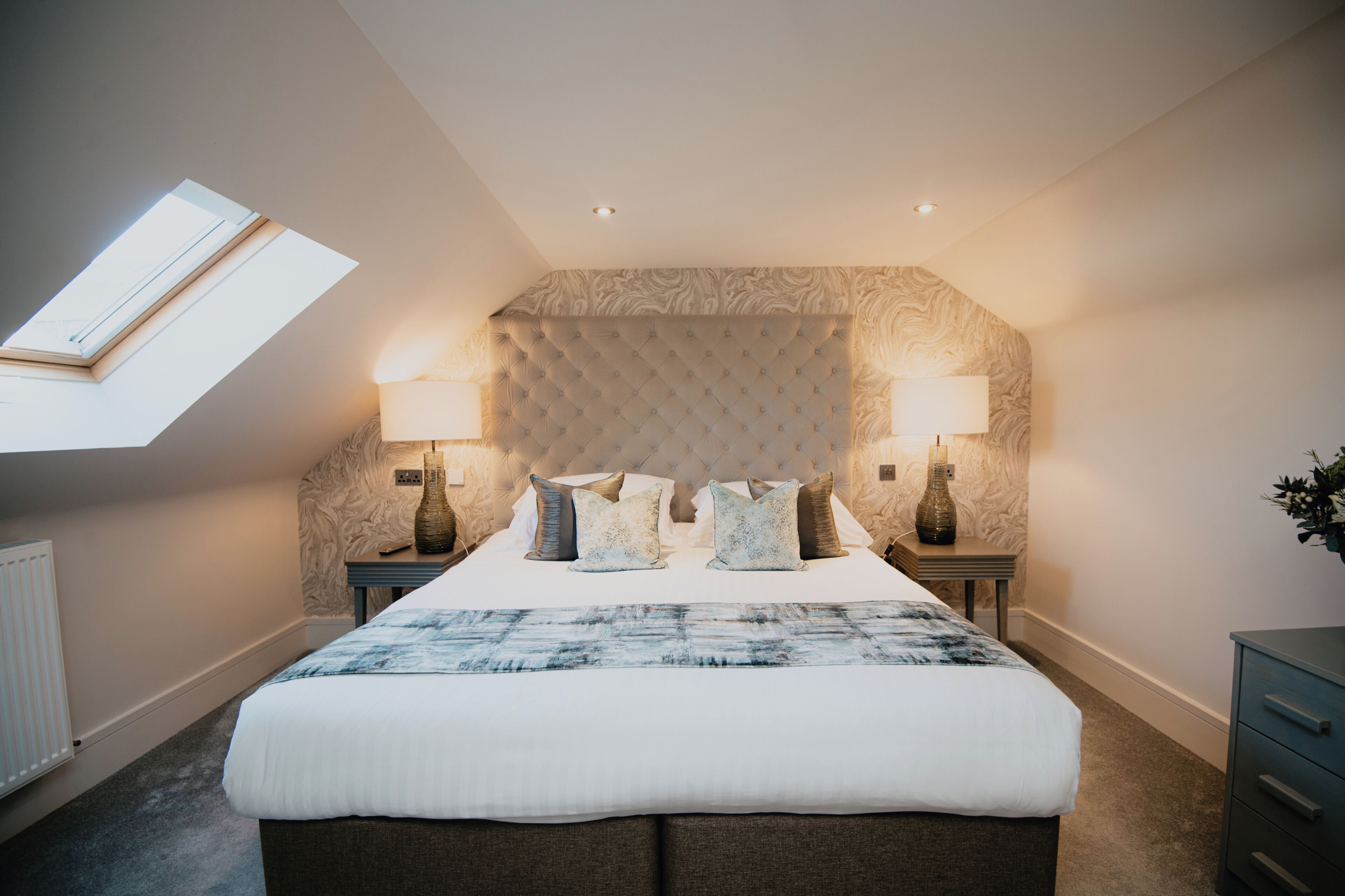 A bedroom with a large bed, two bedside tables, a skylight, and a decorative headboard.