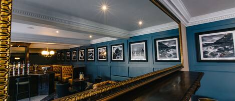 A bar area with a long counter, framed pictures on the wall, and a large mirror reflecting the room.