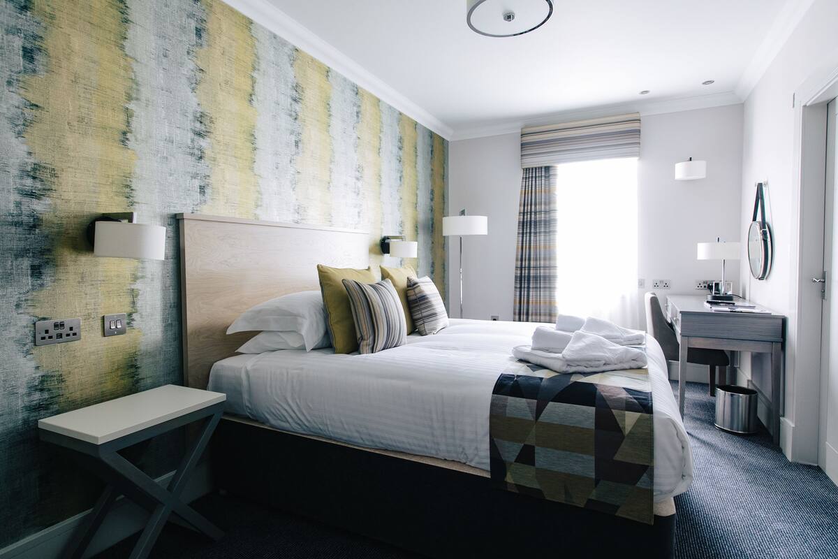 A hotel room with a large bed, bedside tables, a desk, and a window with curtains.