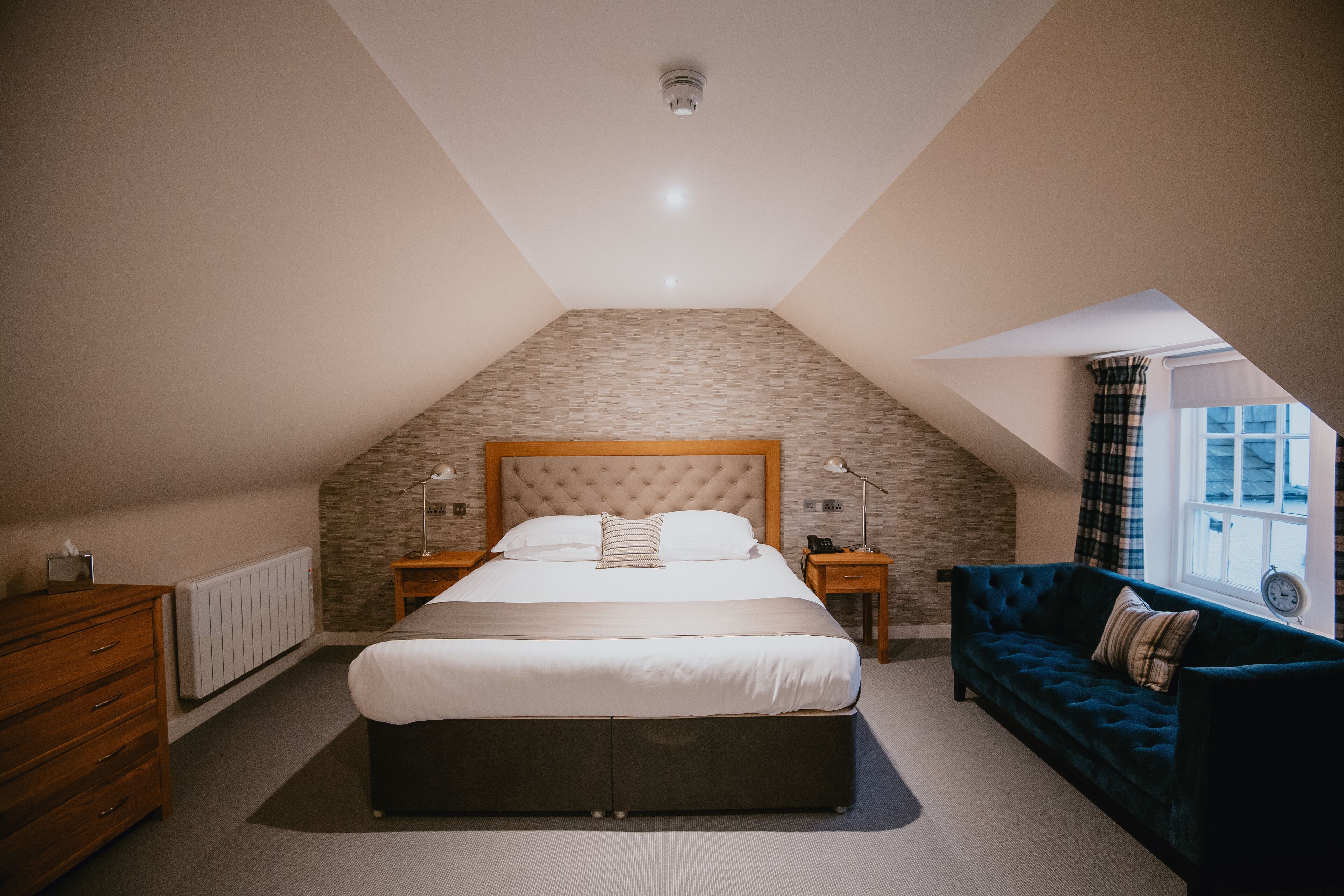 A bedroom with a large bed, a wooden dresser, a dark blue sofa, and a stone-patterned wall.