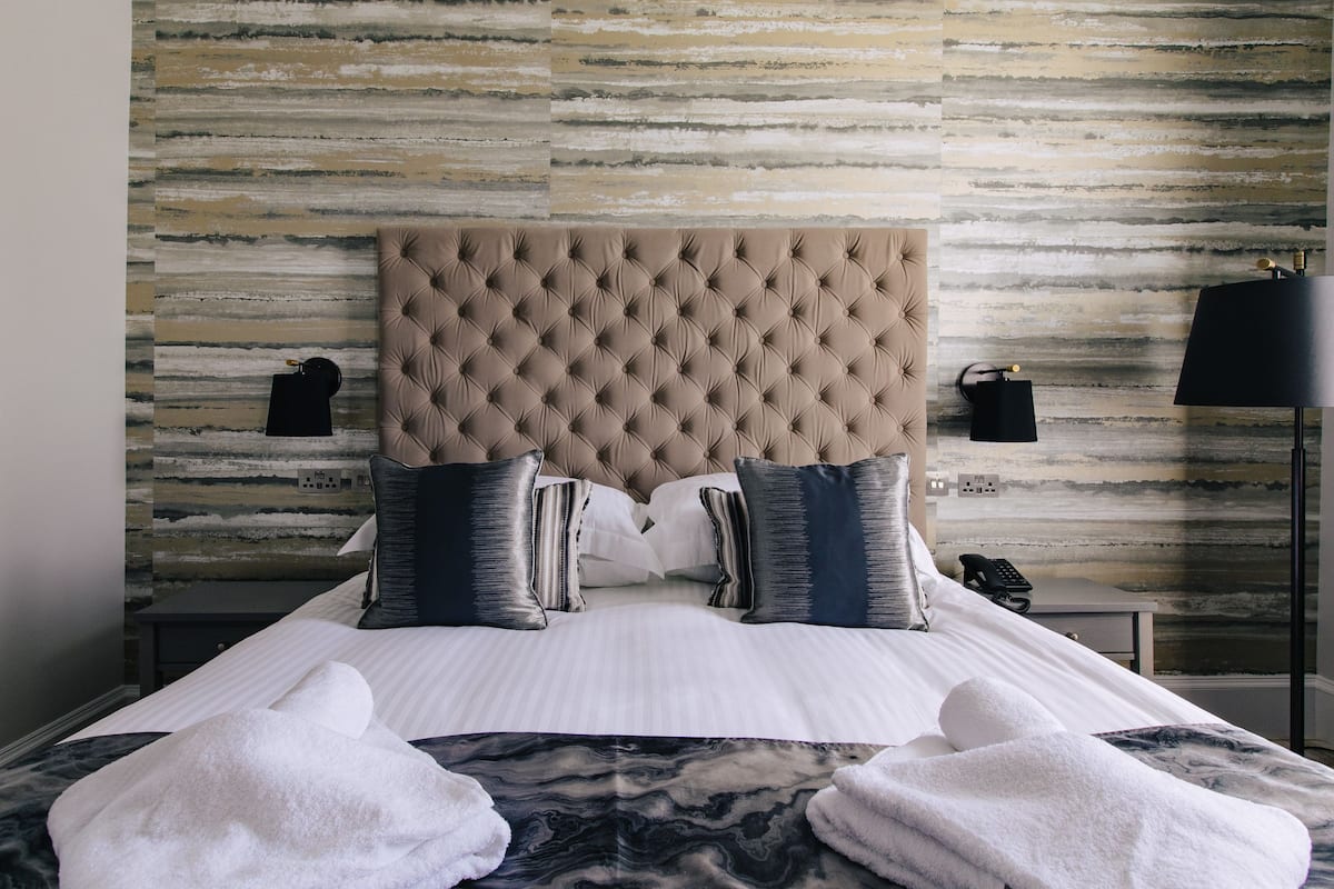 A hotel room with a tufted headboard, two bedside tables with lamps, a bed with white linens, and a marble-patterned bedspread.