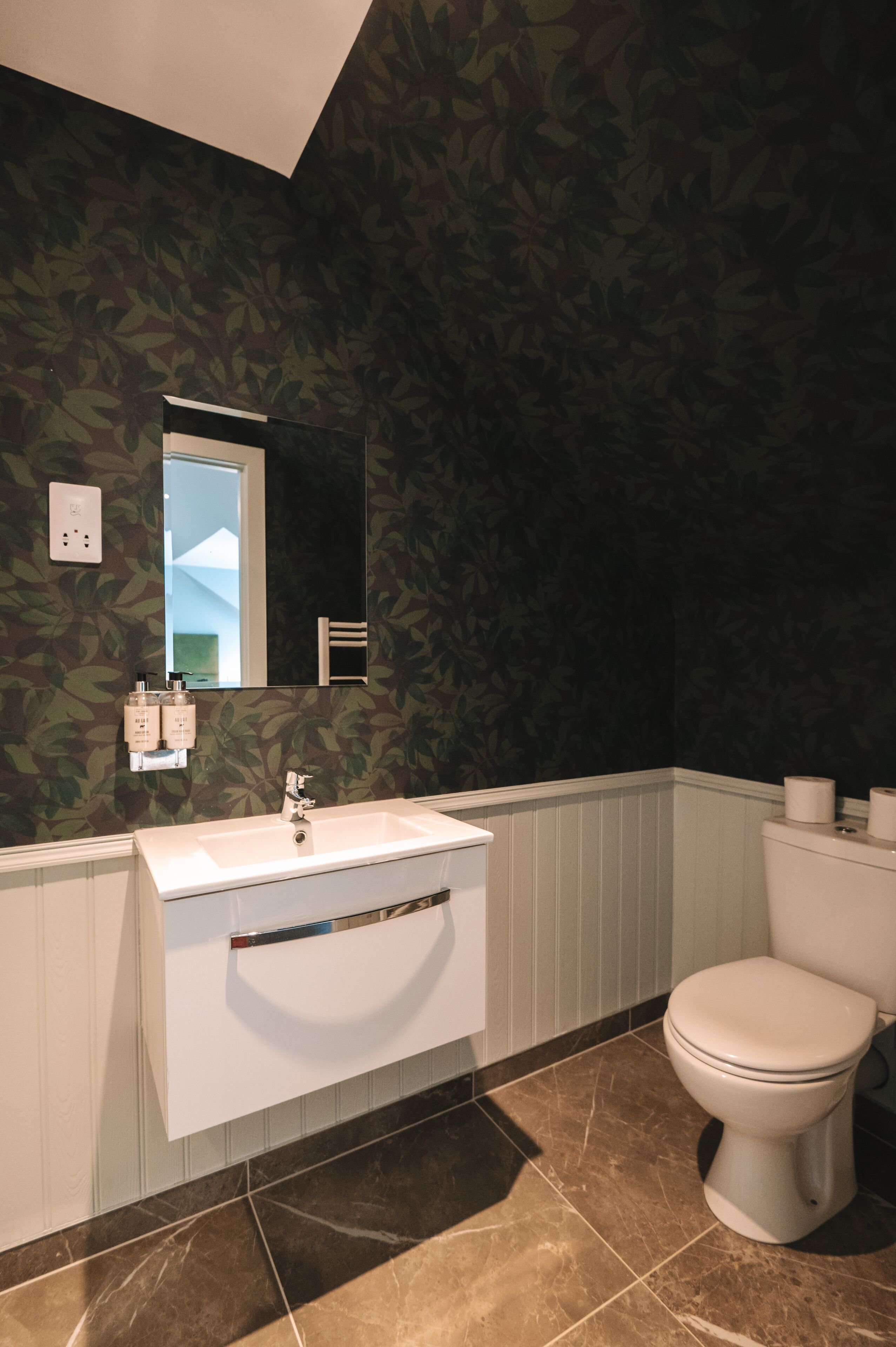 Un baño con lavamanos, espejo e inodoro blancos.
