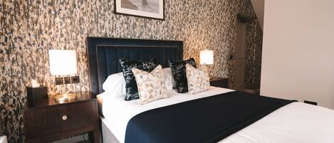 Un lit bien fait, avec une tête de lit sombre, deux tables de chevet avec des lampes et un papier peint à motifs.