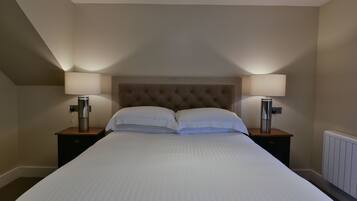 Una cama bien hecha con dos lámparas de noche y un calefactor en la pared.