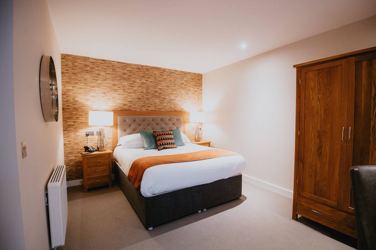 A bedroom with a bed, wooden headboard, nightstands, a wardrobe, and a radiator.