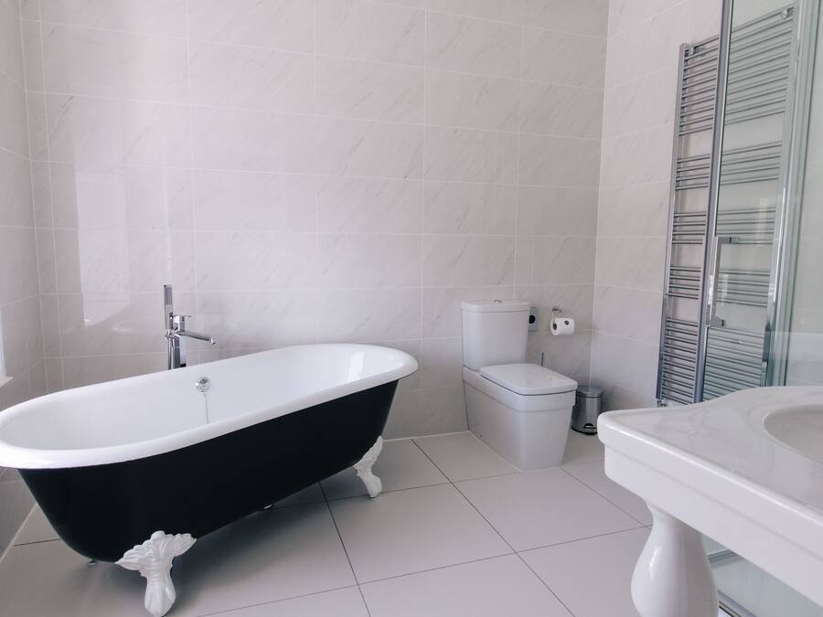 Une salle de bain avec une baignoire noire et blanche, des toilettes et une cabine de douche en verre.