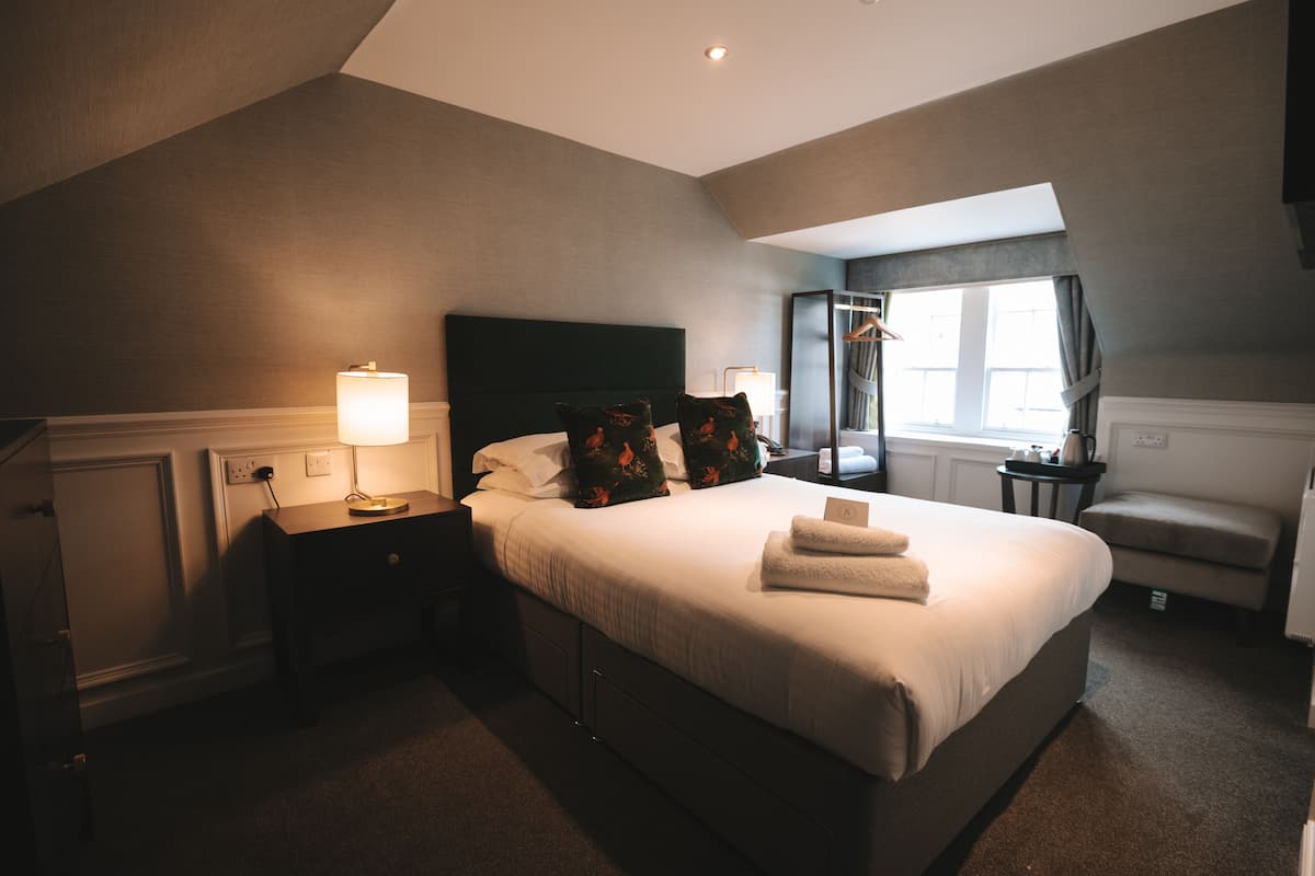 A hotel room with a large bed, a bedside lamp, a small table, and a chair.