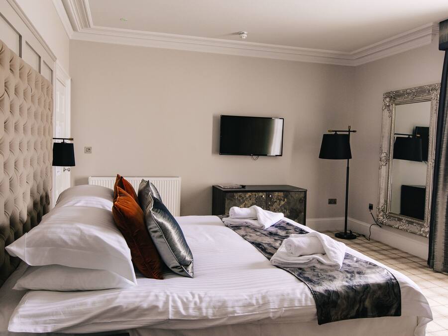 A hotel room with a large bed, a television, a mirror, and a radiator.