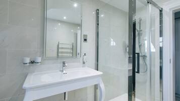 Un baño moderno con un lavabo blanco, una cabina de ducha con mampara de cristal y un espejo grande.