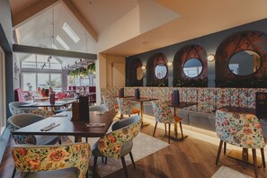 A modern restaurant with floral-patterned chairs and tables, a high ceiling with skylights, and a view of the outside. - The Seafield Arms (Buckie)