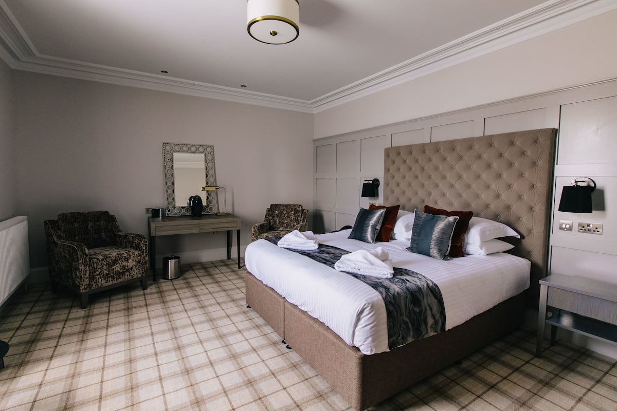 A hotel room with a large bed, two armchairs, a dresser, and a mirror.