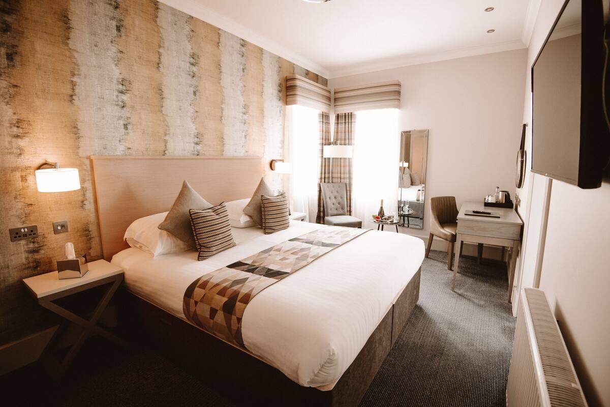 A hotel room with a large bed, bedside tables, a desk, and a mirror.