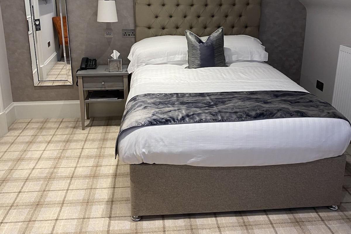 A bedroom with a large bed, a nightstand, a mirror, and a lamp.