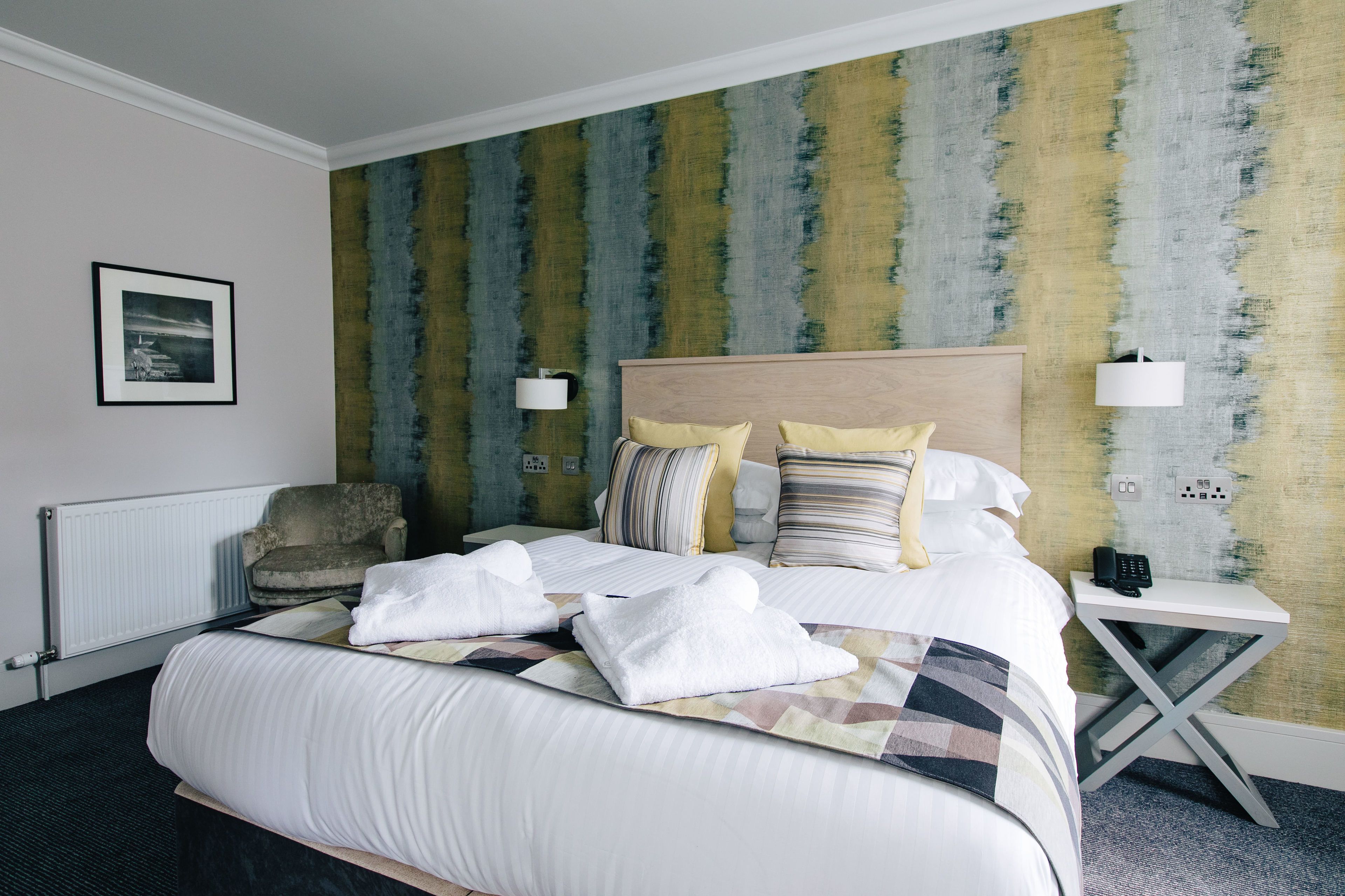 A hotel room with a large bed, a chair, a bedside table with a lamp, and a wall with a textured pattern.