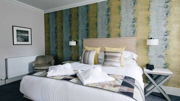 A hotel room with a large bed, a chair, a bedside table with a lamp, and a wall with a textured pattern.