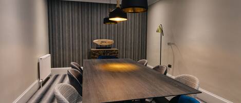 Uma sala de jantar moderna com uma mesa de madeira, cadeiras estofadas em azul e cinza, e luminárias pendentes.