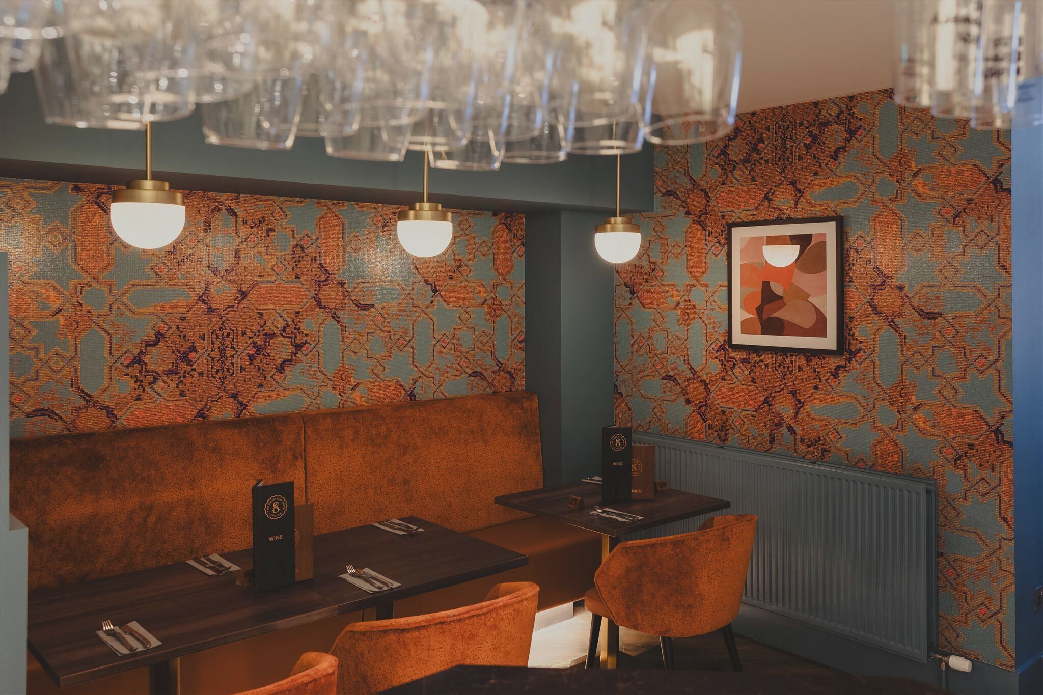 Un restaurant amb paper pintat, seients taronja i lustres de vidre penjants.