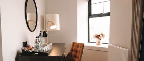 Une chambre d’hôtel avec un bureau en bois foncé, une chaise marron, un miroir, une lampe et une fenêtre donnant sur des fleurs.