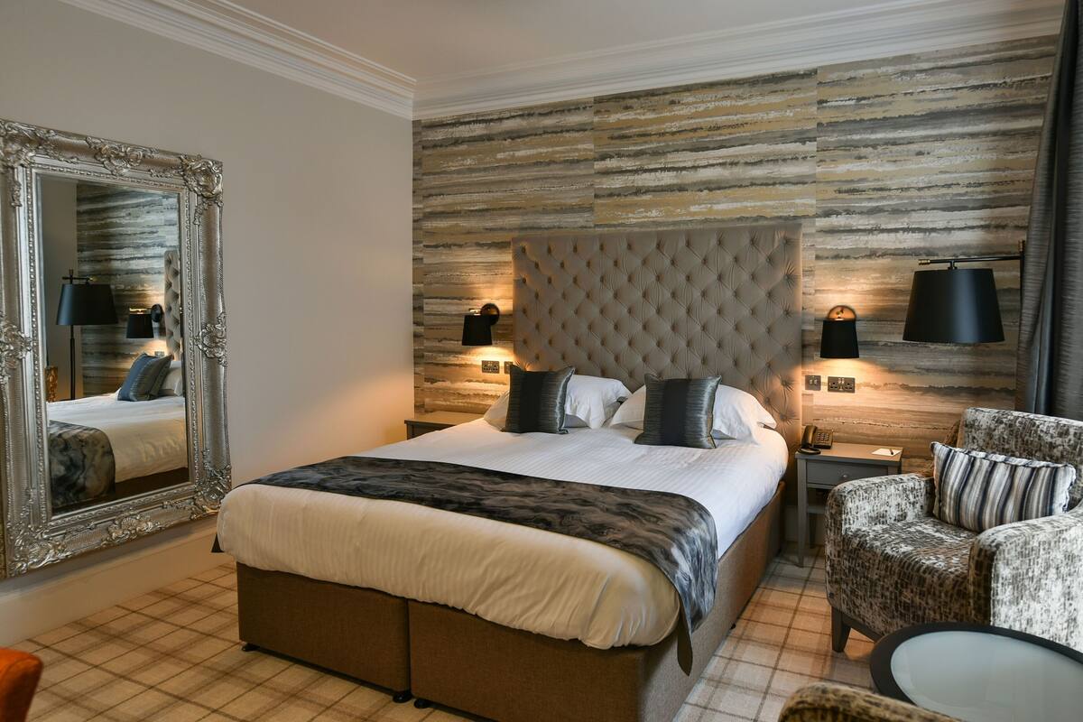 A bedroom with a large bed, a tufted headboard, two bedside lamps, a chair, and a mirror.
