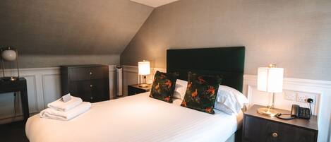 A neatly made bed with pillows, a bedside lamp, and a telephone on a nightstand.