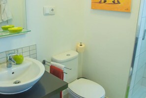 Une salle de bain avec un lavabo blanc, des toilettes et une étagère en verre sur laquelle sont posés des bols.