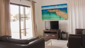 A living room with a large TV, a sofa, and a painting of a pier.