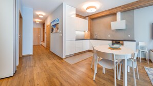A modern kitchen with white cabinets, a wooden countertop, and a dining area with a round table and white chairs. - Apartamenty Sun & Snow Jelitkowska (Gdansk)