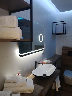 A modern bathroom with a built-in sink, a mirror with a circular light, and neatly stacked towels. - Apartments Ella (Split)