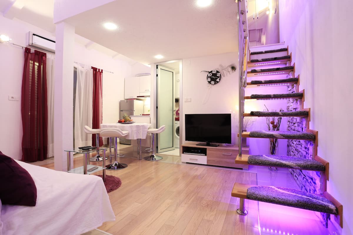 A modern living room with a staircase, a TV, and a dining area.