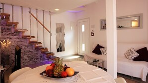 Una sala de estar moderna con una escalera, una mesa de comedor con fruta, un sofá y un televisor.
