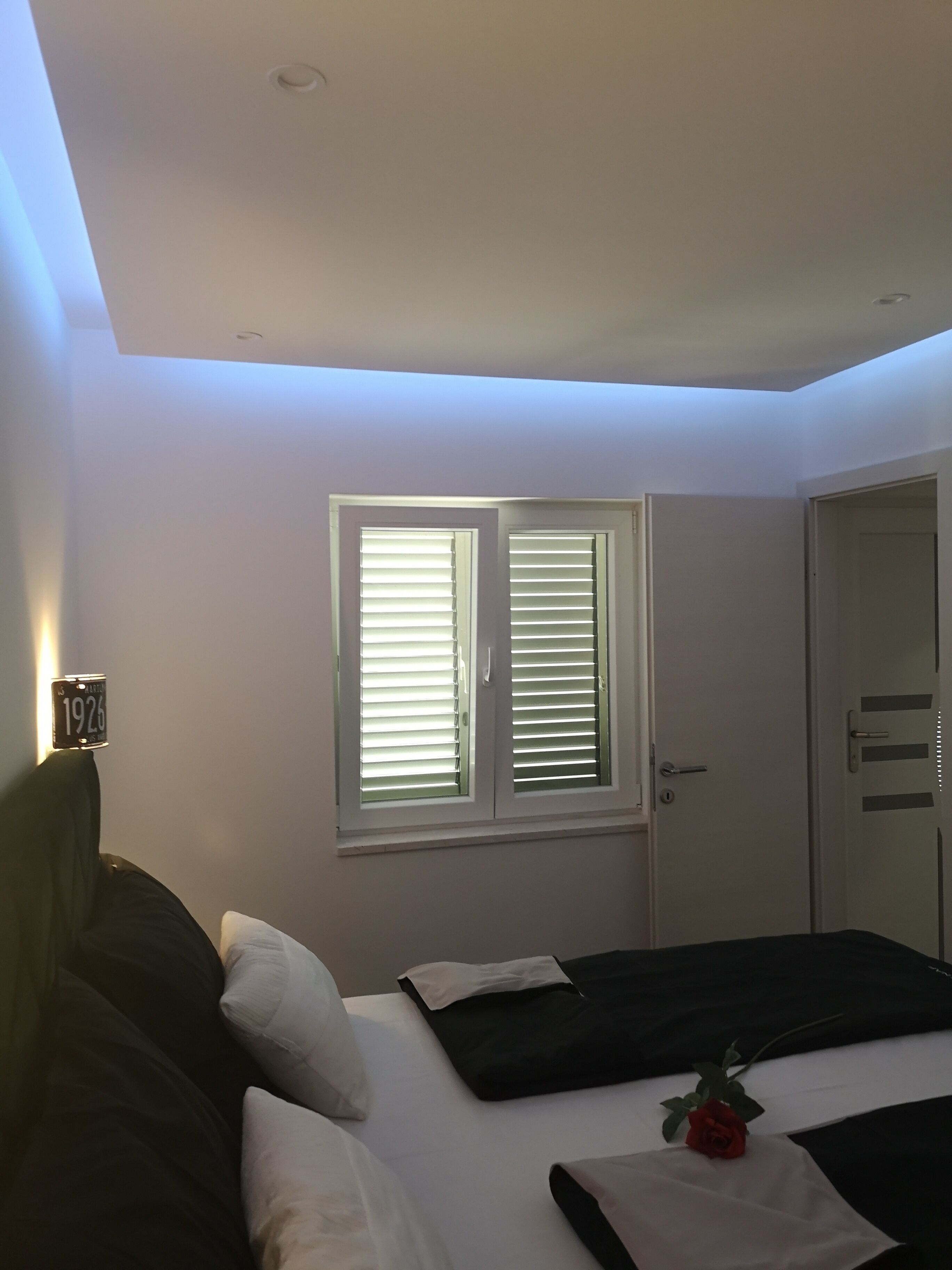 Un dormitorio con una cama, una ventana con persianas, una puerta y una lámpara fijada a la pared.